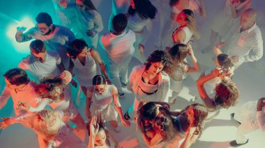 Parlak sahne ışığı altında beyaz partide dans eden kalabalığın en üst görüntüsü. Sosyal yaşam tarzı kültürü kavramı, modern neslin kolektif enerjisi, eğlence ve etkinlikler için ticari görseller.