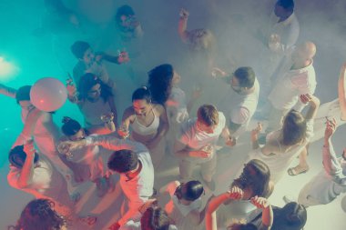 Neşeli beyaz partisinde kalabalık dans edip kadehler kaldırıyor. Yaşam tarzı kutlamaları, gece hayatı kültürü ve eğlence için dinamik görseller veya etkinlik tanıtımı kavramı.