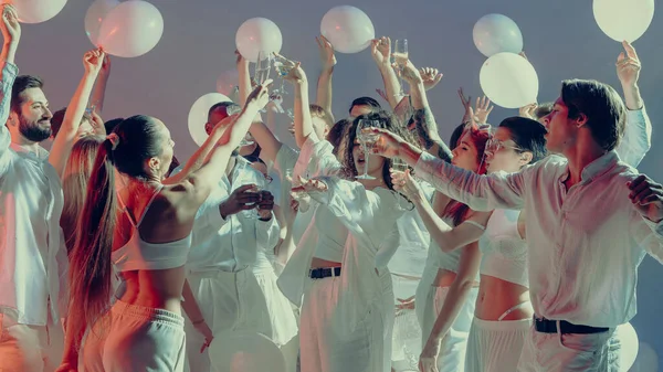 Beyaz sevgililer günü partisini kutlayan neşeli kalabalık birlik içinde kadehler kaldırıyor. Paylaşılan mutluluk kavramı, modern kutlama kültürü ve duygu yoluyla sosyal bağlantı..