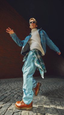 Kot ceketli genç adam modern bir tavırla şehir kemerinin altında güvenle yürüyor. Gençlik sokak modası ve şehir kültüründe motivasyon, tarz ve kişisel kimlik kavramı.