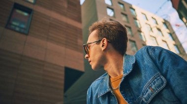 Kot ceketli, sarı kazaklı, yüksek binaların arasında yan bakan bir adam. Yaşam tarzı kavramı, şehir kültürü, moda, teknoloji iletişimi, pazarlama tasarımı.