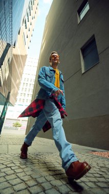 Kot ceketli ve güneş gözlüklü uzun binaların arasında yürüyen bir adam. Sokak modası, sosyal medya etkisi, teknoloji yaşam tarzı, refah psikolojisi ve kentsel eğitim kavramı.