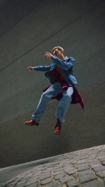 Uzun taş duvarlar arasında kot ceketli ve botlu bir adam zıplıyor. Yaşam tarzı refahı kavramı, sokak modası, fiziksel ifade, dijital medya iletişimi ve seyahat kültürü.