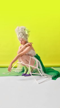 Sarı arka planda çömelmiş yeşil-beyaz Marie Antoinette kostümlü Rococo kadın. Moda kampanyası kavramı, medya reklamları, tarihsel stil eğitimi ve dijital sanat baskıları.