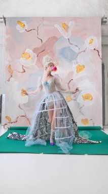 Marie Antoinette karakterinde çiçeklerin önünde pembe sakız üfleyen oyuncu kadın. Lüks yaşam tarzı reklamcılığı, içecek ve güzellik markası kavramı ve medya kampanyaları.