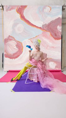 Marie Antoinette karakterindeki zarif kadın soyut arka planda tüylü süslemeli mavi kokteyl tutuyor. Lüks içecek hikâyesi kavramı, sinematik moda markalaşması, yaşam tarzı zarafeti..