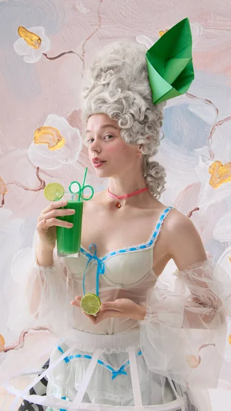 Marie Antoinette gibi giyinmiş zarif bir kadın elinde limon dilimleri ve yumuşak bir gülümsemeyle yeşil bir kokteyl tutuyor. Koku ve içecek kampanyası kavramı, sinematik yaşam tarzı reklamları ve lüks markalaşma..