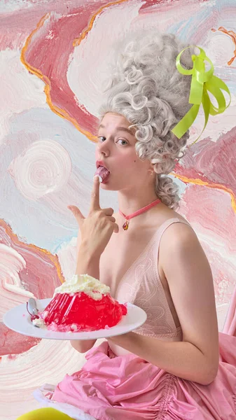Oyuncu rokoko kadın pastel sanatsal arka planda kırmızı tatlıyı tadıyor. Lüks tatlı ve parfüm kampanyası kavramı, sinematik şehvet ve yaşam tarzı markalaşması.