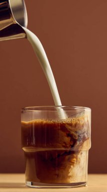 Süt akıntısı koyu espresso ile karıştırılarak yakın plan kremalı girdap ve kontrastı gösteriyor. Kahve işçiliği, içecek markası, lüks yaşam tarzı ve ürün pazarlama kavramı..