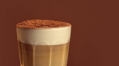 Kakao tozlu latte cam yumuşak köpük desenli ve sıcak kahverengi gradyan arka planlı. Kahveci sanatı, içecek kompozisyonu, mutfak tasarımı ve zarif kafe markası kavramı..