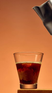 Bardakta kahve, kalın kıvrımlı dokular ve sıcak arka planda metal sürahi. Kahveci sanatı, içecek üretimi, kafe tasarımı ve mutfak markası kavramı..