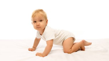 Meraklı bebek beyaz yatakta sürünüyor. Etrafı incelikle ve dikkatle incelikle keşfediyor. Erken çocukluk öğreniminde büyüme, gelişme ve keşif kavramı.