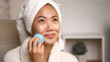 Havluyla yüz masajı yapan bir kadın. Nazikçe gülümsüyor. Cilt bakım teknolojisi kavramı, günlük gençleştirme ve sağlık rutini farkındalıkla bağlantılı..