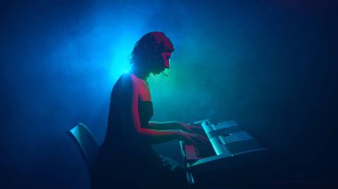 Kadın piyanist mavi ve yeşil ışık altında elektronik klavye çalıyor. Yaratıcı endüstriler için görsel yayın kavramı, sosyal medya kampanyaları ve editör fotoğrafçılığı.