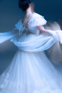 Beyaz terzide dramatik etek kaldırma, ifade edici hareket bulanıklığı ve heykel jesti. Lüks moda markaları, modern dekor görselleri ve hareket terapisi temaları kavramı.