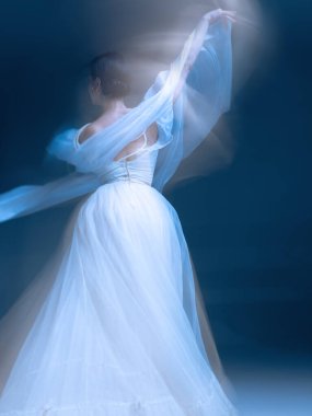 Dansçı yumuşak mavi ışıkta, katmanlı önlük ve hareket bulanıklığında inciler içinde dönüyor. Moda kimliği, vücut güveni ve zarif ritimle duygusal rahatlama kavramı..