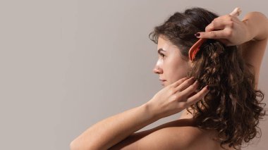 Kıvırcık saçlı kadın saçlarını turuncu tarakla doğal ışıkta çözüyor. Trichology kavramı, kafa sağlığı, ev güzellik bakımı ve günlük bakım için doğal saç bakımı..