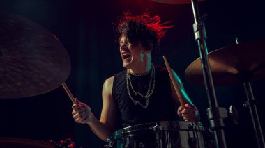 Rock davulcusu tutkulu bir şekilde etkileyici bir yüz ve kırmızı ışık aksanıyla çalıyor. Enerji, duygu, müzik akışı görselleri, editoryal kullanım ve motivasyonel hikaye anlatımı kavramı.