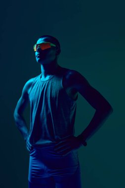 Elleri mavi-yeşil neon ışığın altında duran bir sporcu. Spor kıyafetleri reklamcılığı, fitness koçluğu markalaşması, atlet portföyü tasarımı, motivasyonel spor içeriği kavramı.