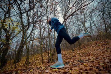 Erkek koşucu orman yamacını aşıyor. Yükselen bir adım ve kendinden emin bir şekilde ileri doğru itiyor. Açık hava sporları, motivasyon uygunluğu görsellik, aktif yaşam ve doğa temelli refah kavramı.