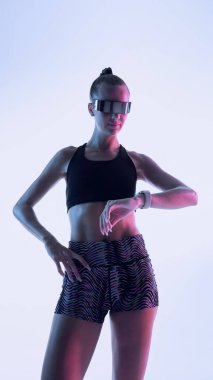 Akıllı vizörle poz veren ve neon ışıklı akıllı kadın atlet. Yüksek teknoloji fitness modası, spor malzemelerinde yenilik ve kendinden emin atletik ruh hali kavramı..