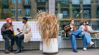 Arkadaşlar kış caddesinde sıcak içeceklerle dışarıda sohbet ediyorlar. Şehir turizmi kavramı, rahat refah anları, sosyal medya hikaye anlatımı ve mevsimlik kahve yeri tanıtımı.