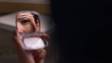 Küçük aynaya bakarken kaşlarını şekillendiren kadın. Günlük güzellik anlayışı, kişisel bakım, cilt bakım alışkanlıkları, kişisel bakım yaşam tarzı ve kozmetik pazarlama.