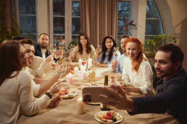 Arkadaşlar yemekte grup selfie 'si için şarap kadehleri kaldırıyor. Sosyal medya yaşam tarzı içeriği, modern kutlamalar, arkadaşlık pazarlaması ve günlük etkinlik tanıtımı kavramı.