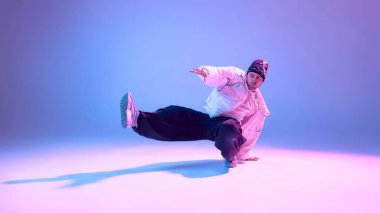 Erkek break dansçı stüdyo ortamında tek ayak üzerinde dengede duruyor. Aktif yaşam tarzı tanıtımı, spor markalaşması, kişisel eğitim programları, motivasyon görselleri ve atletik performans içeriği kavramı.