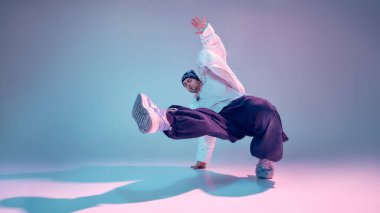 Sokak dansçısı renkli stüdyoda etkileyici bir hareket sergiliyor. Yaratıcı performans görselleri, yaşam tarzı markalaşması, modern spor promosyonu ve gençlik odaklı reklam içeriği kavramı.