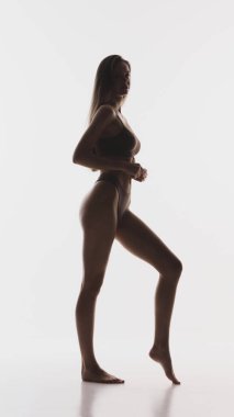 Atletik kadın vücut silueti stüdyo arka planında tam uzunlukta. Fitness markası kavramı, vücut pozitifliği kampanyaları, spor giyim reklamları, sağlık pazarlama görselleri..