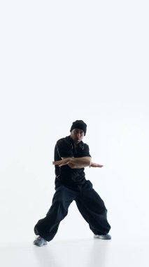 Beyaz arka planda çapraz kollarla güçlü poz veren çağdaş bir dansçı. İç güç kavramı, kendine güven, sakin güç ve modern markalaşma görselleri için kontrollü duygu..