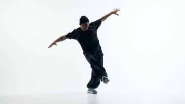 Erkek sokak dansçısı stüdyoda tek bacağı üzerinde dengede duruyor. Spor ve yaşam tarzı iletişimi için beden kontrolü, koordinasyon, güven ve dinamik denge kavramı.