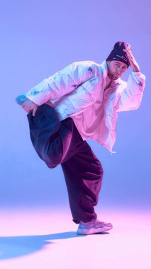 Erkek hip hop dansçısı stüdyoda tek bacağının üzerinde mavi mor ışıkla dengede duruyor. Sokak dansı eğitimi, vücut kontrol pratiği, modern koreografi, yaratıcı performans, kentsel kültür tanıtımı kavramı.
