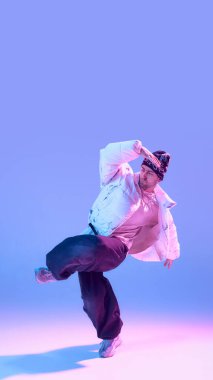 Neon Stüdyo ışıklandırmasında kaldırılmış koluyla poz veren erkek sokak dansçısı. Çağdaş dans tarzı, serbest stil ifadesi, yaratıcı güven, gençlik kültürü görselleri ve sanatsal hareket kavramı.