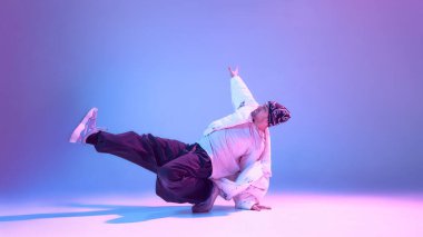 Sokak dansçısı, stüdyo ışıklandırmasında düşük denge pozisyonunda duruyor. Kontrollü hareket, dans eğitimi odak noktası, beden bilinci, çağdaş koreografi ve anlamlı durgunluk kavramı.