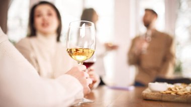 İçeride rahatlamış grup tadımına odaklanmış şarap kadehi. İçecek markası kavramı, yaşam tarzı içeriği, alkol reklamı, kaliteli içki tanıtımı ve modern iç mekanda sosyal atmosfer.