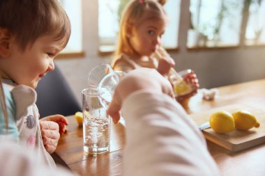 Çocuk masada limonla su içmeyi öğreniyor. Erken sağlıklı alışkanlıklar, hidrasyon eğitimi, aile rutini, temiz su tüketimi ve çocukluk sağlığı kavramı.