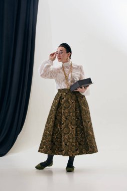 Stüdyoda dantelli bluz ve ipek etekli klasik bir kadın kitap tutuyor. Moda hikaye anlatımı, entelektüel kadınlık, şair özünde estetik, editoryal stil, klasik gardırop ilhamı..