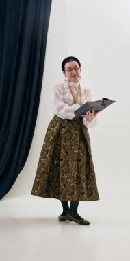 Bağcıklı bluz ve ipek etek giyen klasik bir kadın stüdyoda nazik bir şekilde kitap okuyor. Moda hikaye anlatımı kavramı, entelektüel kadınlık, klasik gardırop, editoryal ve kültürel kullanım.