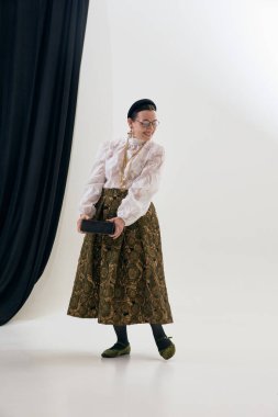 Dantel bluzlu, desenli etekli, büyük bir kitap tutan olgun bir kadın. Yaşam tarzı moda anı, şair özlü güzellik, klasik kadınlık, reklam ve marka kullanımı için editoryal tasvirler.