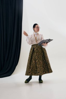 Klasik şair kıyafetiyle kitap okuyan zarif, olgun bir kadın. Eğitim yaşam tarzı kavramı, entellektüel moda, kültürel hikaye anlatımı, reklam ve yayın kullanımı için editoryal betimleme.