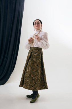 Klasik kıyafetlerini stüdyoda gösteren zarif, klasik bir kadın. Klasik moda ayrıntıları, kadın güveni, retro ayakkabı sunumu, moda ve yaşam tarzı kullanımı için zamansız stil kavramı.