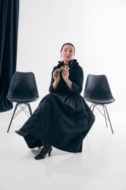 Siyah elbiseli zarif bir kadın stüdyoda opera gözlükleriyle oturuyor. Tiyatral moda kavramı, şair ruh hali, rafine kadınlık, kültürel zarafet, editoryal portre tasarımı..