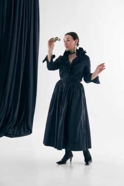 Siyah fırfırlı elbiseli, elinde opera dürbünü olan klasik bir kadın. Moda editör stili kavramı, tiyatro estetiği, retro zarafet, kültürel etkinlikler promosyon, lüks yaşam tarzı görselleri.