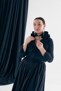 Siyah klasik elbiseli zarif bir kadın kolyeyi ayarlıyor. Moda reklamcılığı, mücevher tanıtımı, klasik güzellik markası, butik pazarlama, zamansız kadınsı tasvirler..