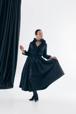 Siyah elbiseli kadın zarif bir stüdyo pozu veriyor. Zamansız moda kavramı, kadın hareketi, klasik siluetler, şair estetiği ve sanatsal yazı stili..