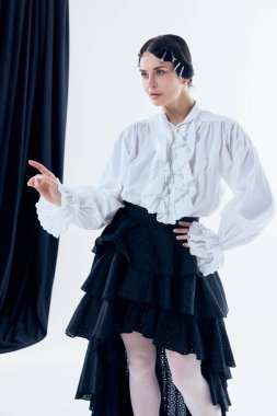Beyaz fırfırlı bluzlu ve şair estetiğini gösteren siyah etekli bir kadın. Tiyatral moda kavramı, modern romantik stil, yaratıcı markalaşma, butik kampanya ve sanatsal içerik.
