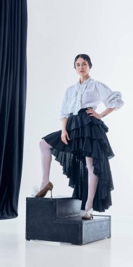 Beyaz stüdyo içinde siyah basamaklarda poz veren şair kıyafetli kadın model. Moda tasarımı, tasarım koleksiyonu tanıtımı, premium tasarım ve giyim pazarlama içeriği kavramı.