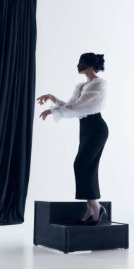 Dantel peçeli bir kadın platformda poz veriyor ve elleri stüdyoda ifade ediyor. Performanstan esinlenilmiş moda görselleri, yaratıcı kampanya üretimi ve yenilikçi stil içeriği kavramı.